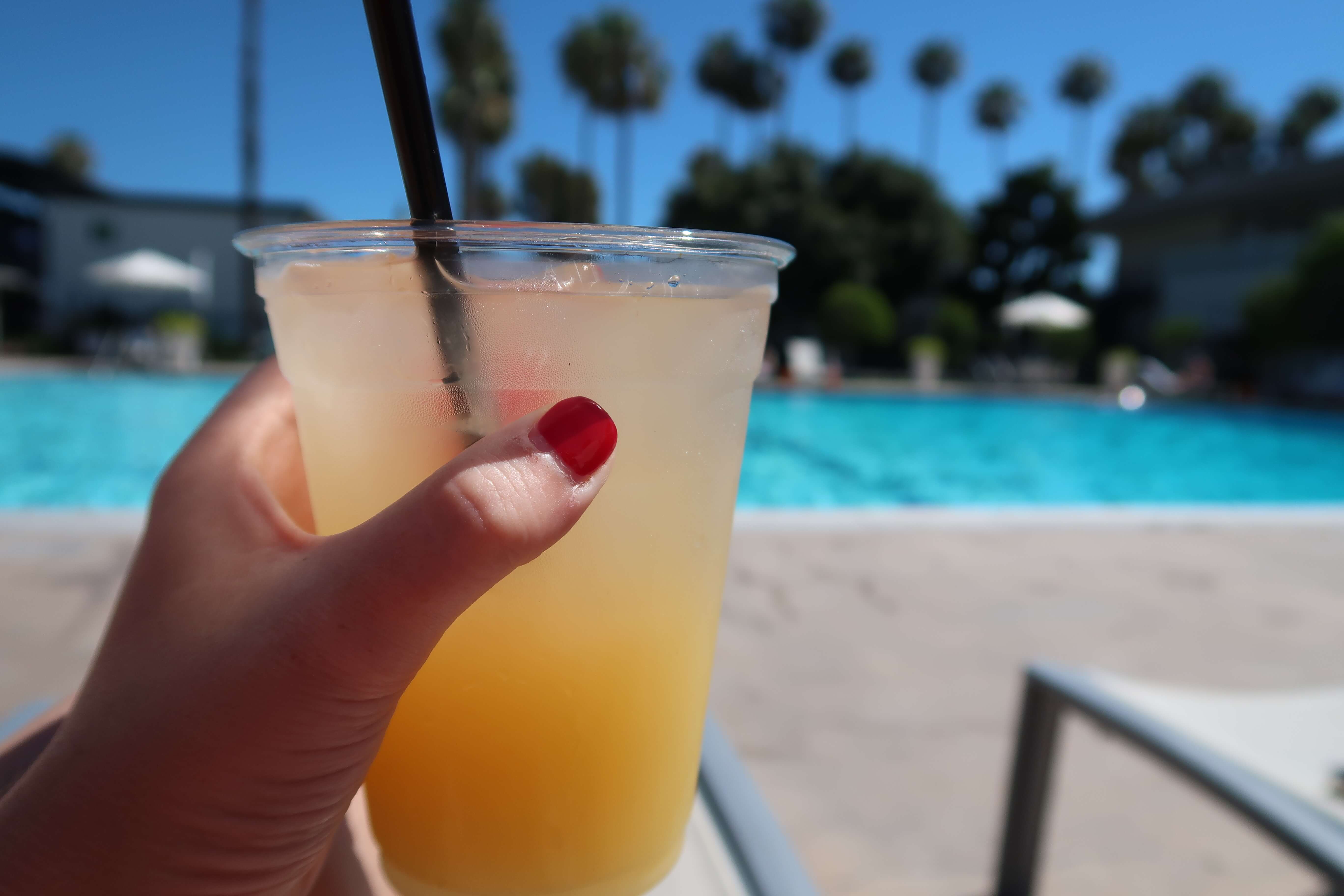 Holding cocktail drink up to pool at The Anaheim Hotel